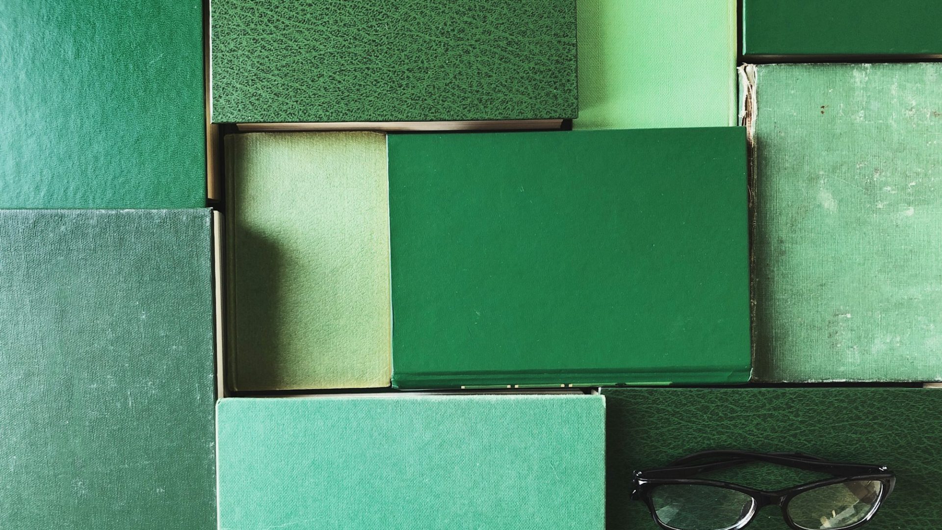 green-books-laying-flat-on-a-table-in-a-pattern-with-reading-glasses-on-top.jpg